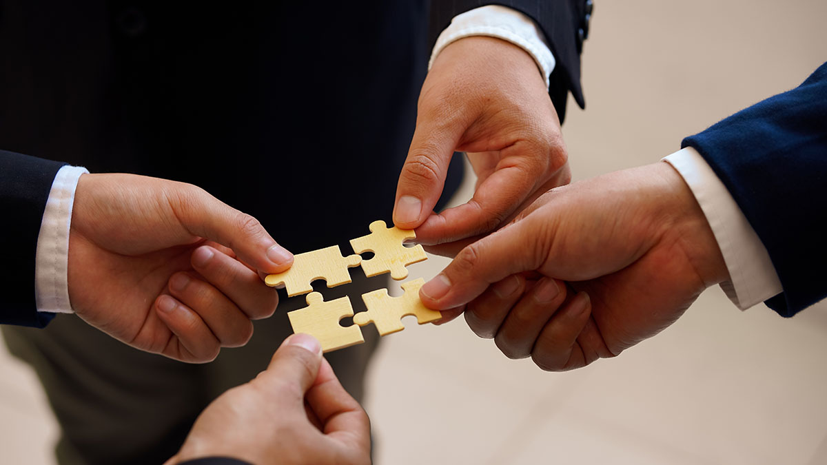 Cuatro manos en traje de oficina unen piezas de un puzzle