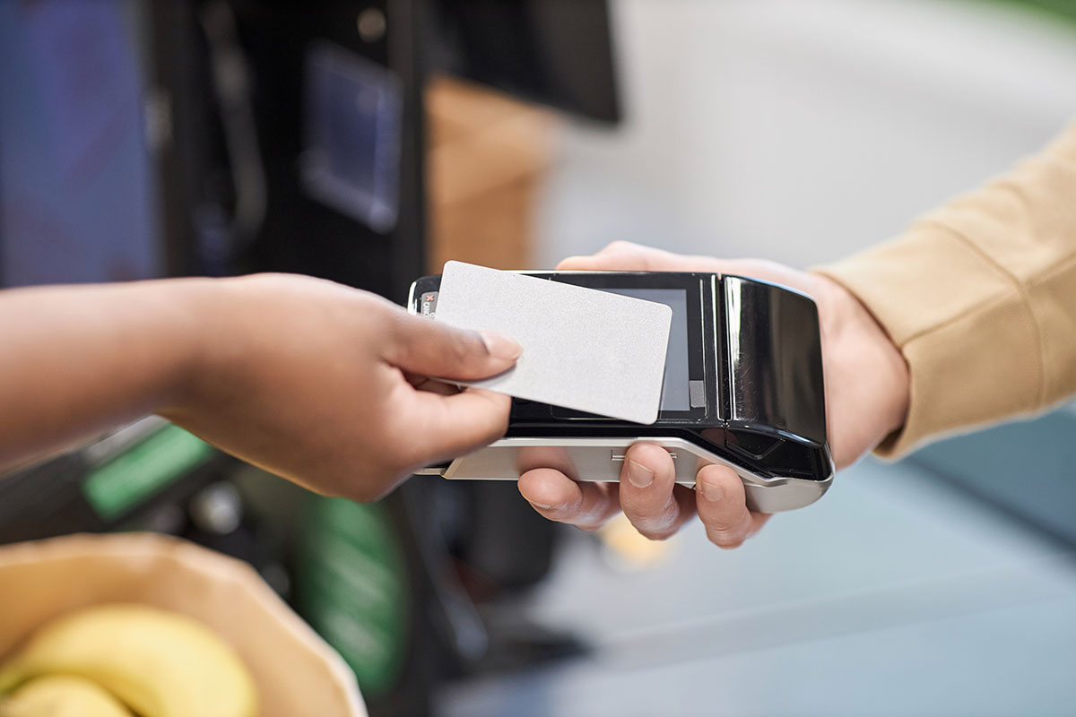 Mano con móvil realiza su pago sobre un datáfono en un establecimiento.