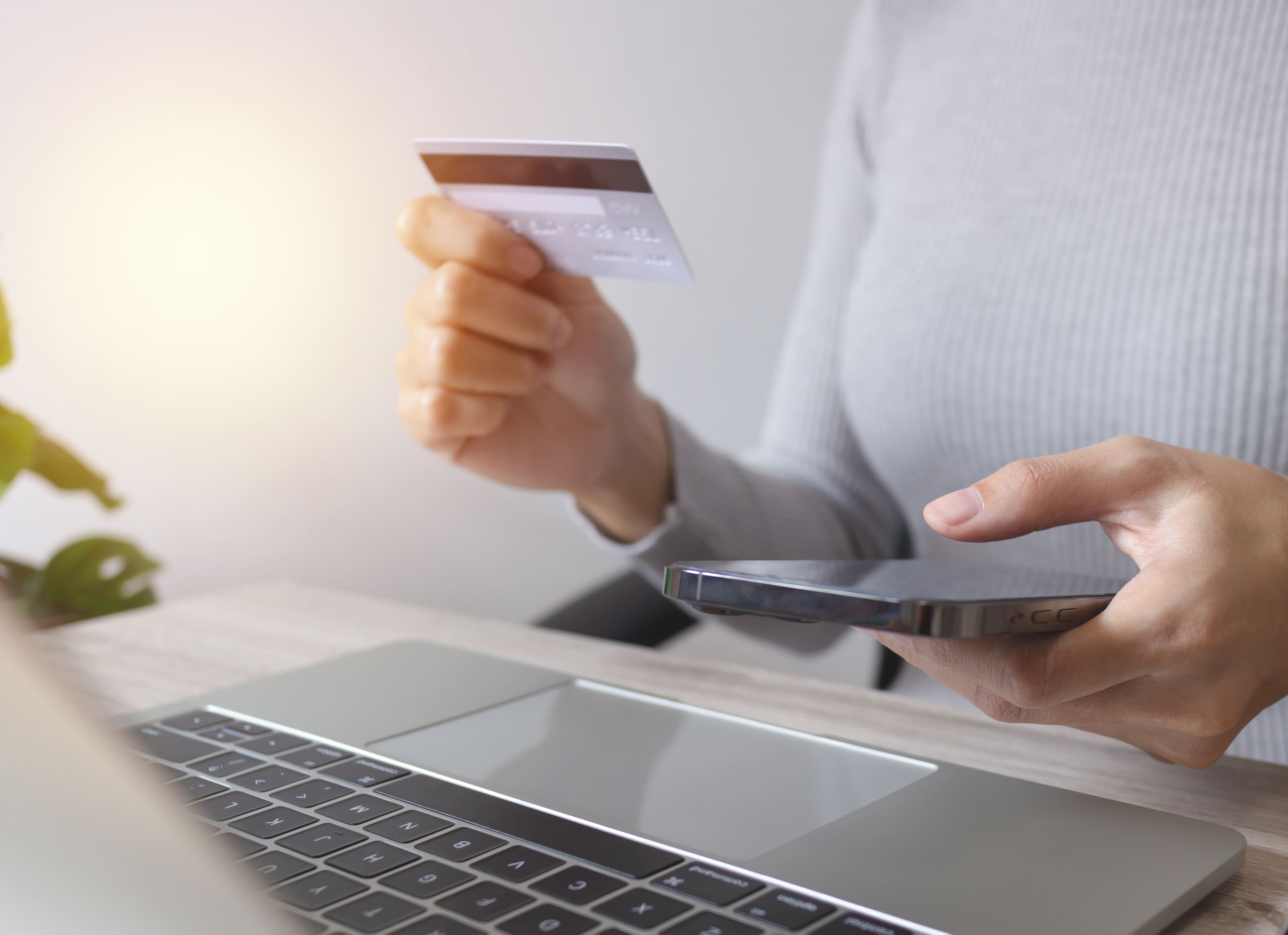 Imagen recortada de una mujer haciendo una compra online con su tarjeta, móvil y pc